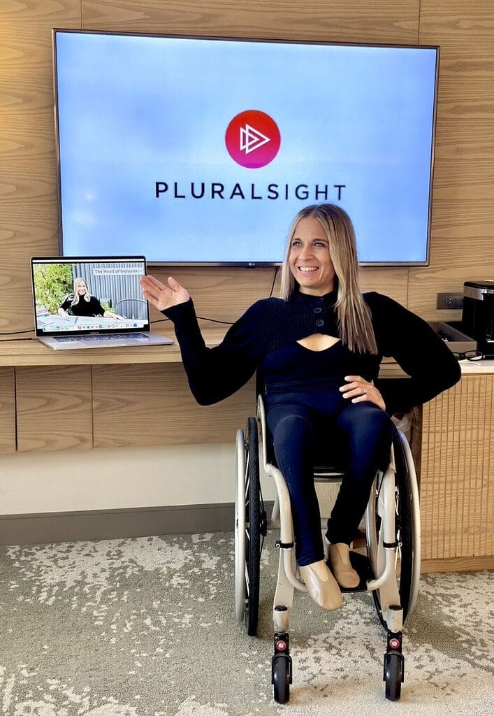 Alycia sitting in wheelchair wearing black pointing at the Pluralsign screen